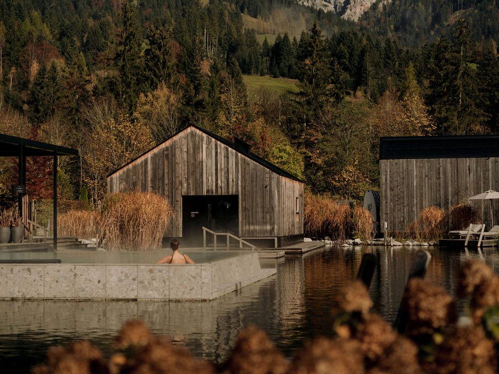 Blick über den Seepool zum Seehaus und zur Leoganger Stadlsauna, eingebettet in die herbstliche Natur mit den Leoganger Steinbergen im Hintergrund.
