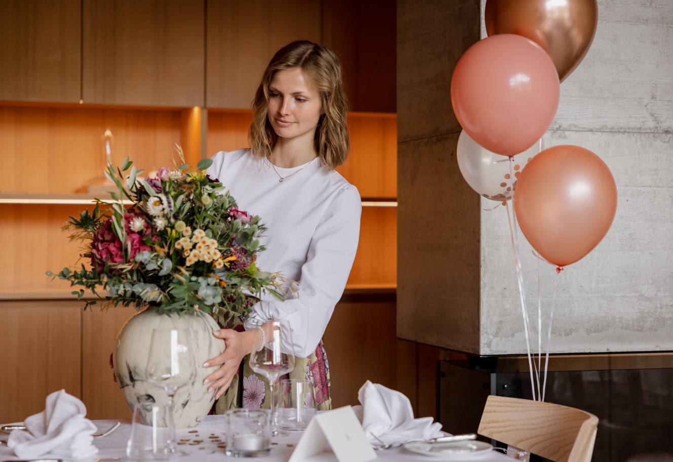 A member of the Glücksbringer team arranges a lush autumn flower bouquet on an elegantly set table for a special celebration.
