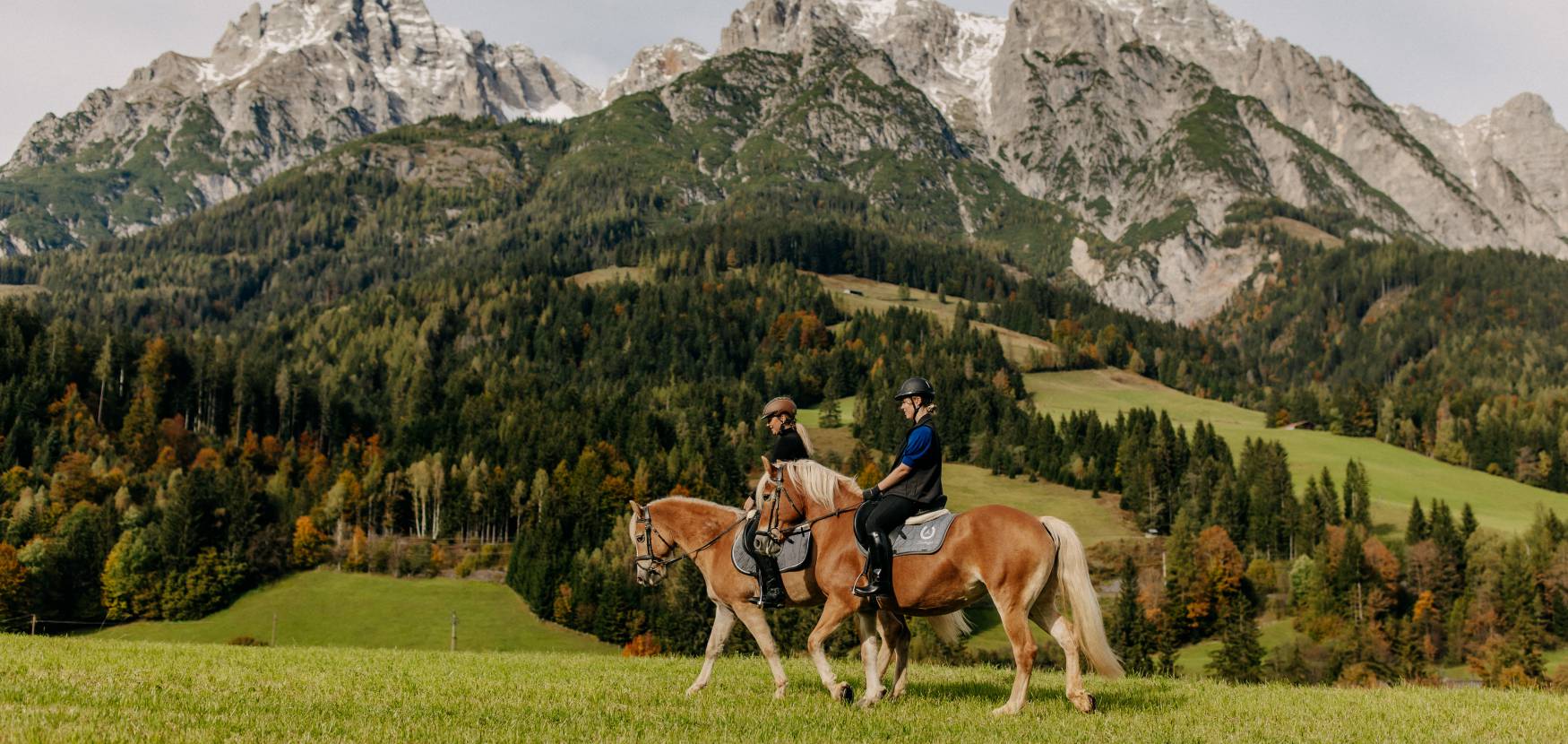 Two riders on Haflinger horses with an autumn mountain backdrop in Leogang