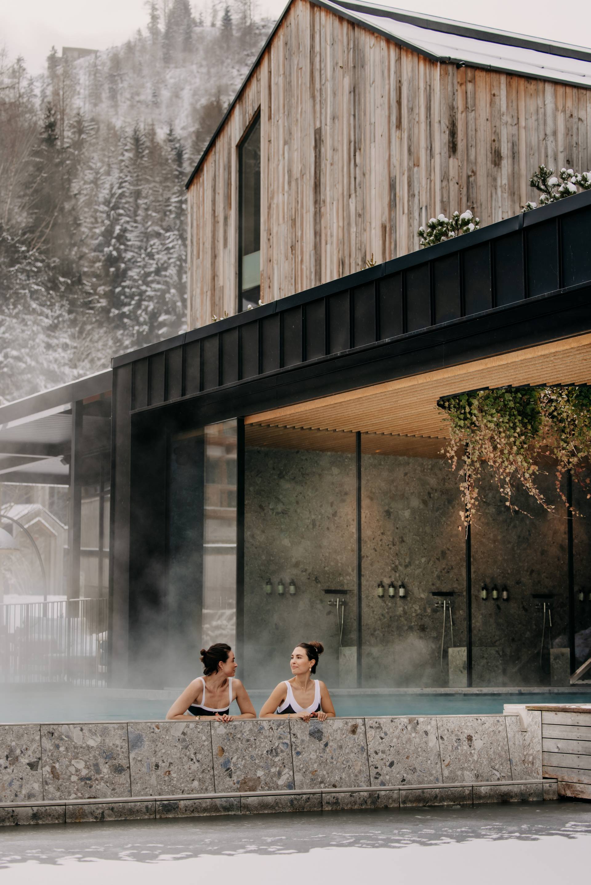 Zwei Frauen entspannen im Seepool des Naturhotel Forsthofgut an einem winterlichen Tag.