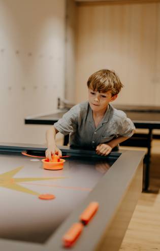 Junge spielt Airhockey an einem modernen Spieltisch mit orangefarbenem Schläger und Puck.