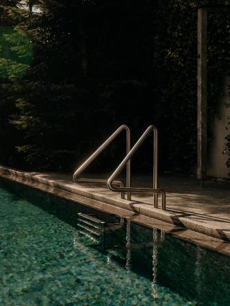 Sportpool mit Liegefläche, Sonnenschirmen und Blick auf die Leoganger Steinberge im Sommer.