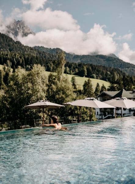 Woman in the 25m sportpool enjoing the view of the Leoganger Steinberge / Naturthotel Forsthofgut Garden loft suit interior