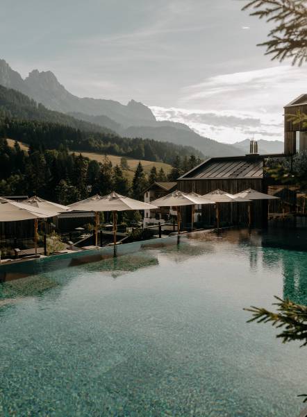Sportpool mit Liegefläche, Sonnenschirmen und Blick auf die Leoganger Steinberge im Sommer.