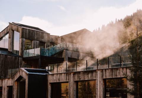 Adults-only area of Naturhotel Forsthofgut with modern wooden architecture and steam rising from the outdoor spa areas.