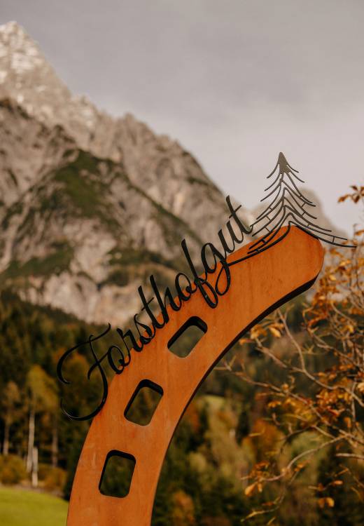 Teil unseres großen Metall-Hufeisens mit dem Schriftzug „Forsthofgut“ vor der herbstlichen Alpenkulisse.