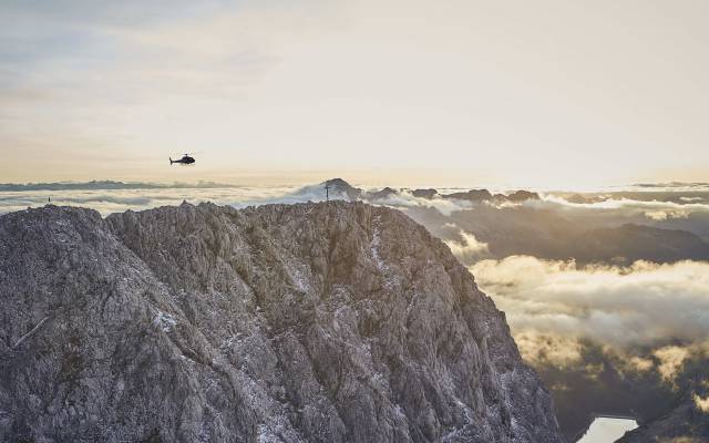 Helicopter flight over snow-covered Alpine peaks at sunset.