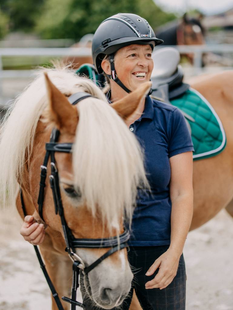 Frau hält Pferd an der Zügel und lacht