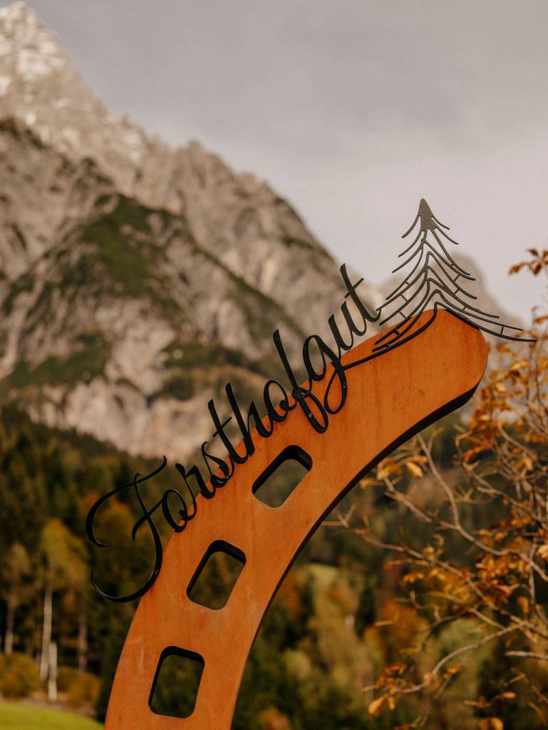 Teil unseres großen Metall-Hufeisens mit dem Schriftzug „Forsthofgut“ vor der herbstlichen Alpenkulisse.