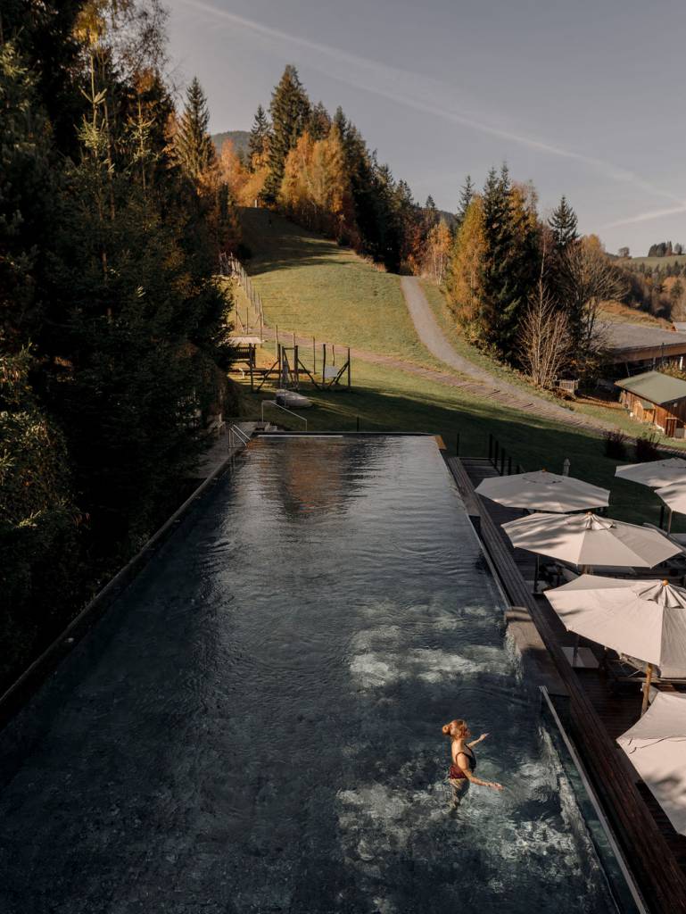 Frau im beheizten Adults-Only-Sportpool mit Blick auf herbstliche Wälder und Wiesen – Wellness und Erholung inmitten der Salzburger Alpen.