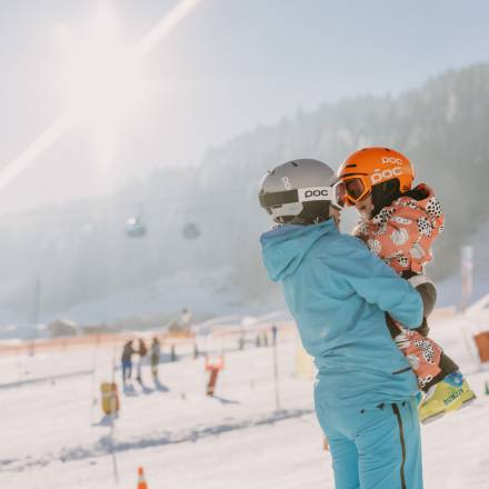 Person hält Kind auf den Armen im Skigebiet