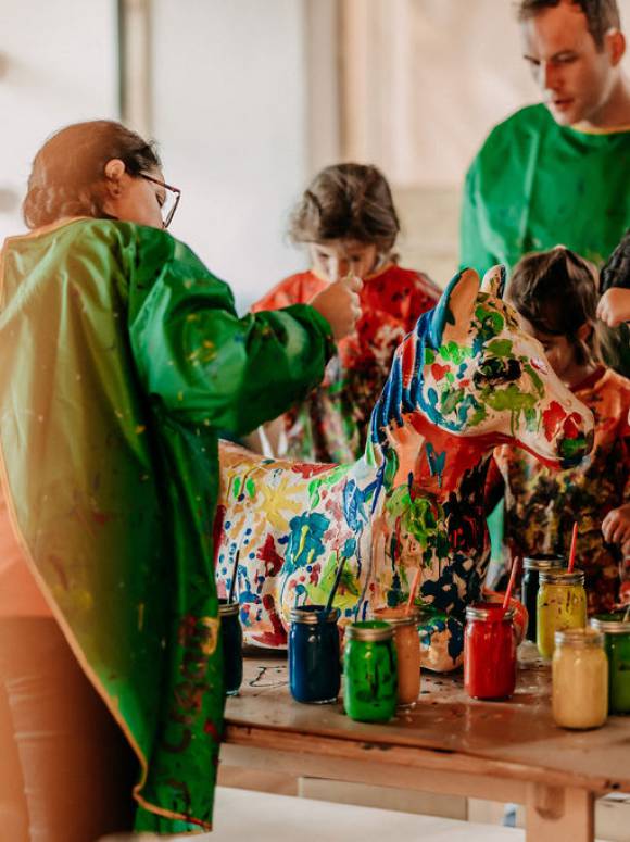 Children at the painting table paint a horse statue