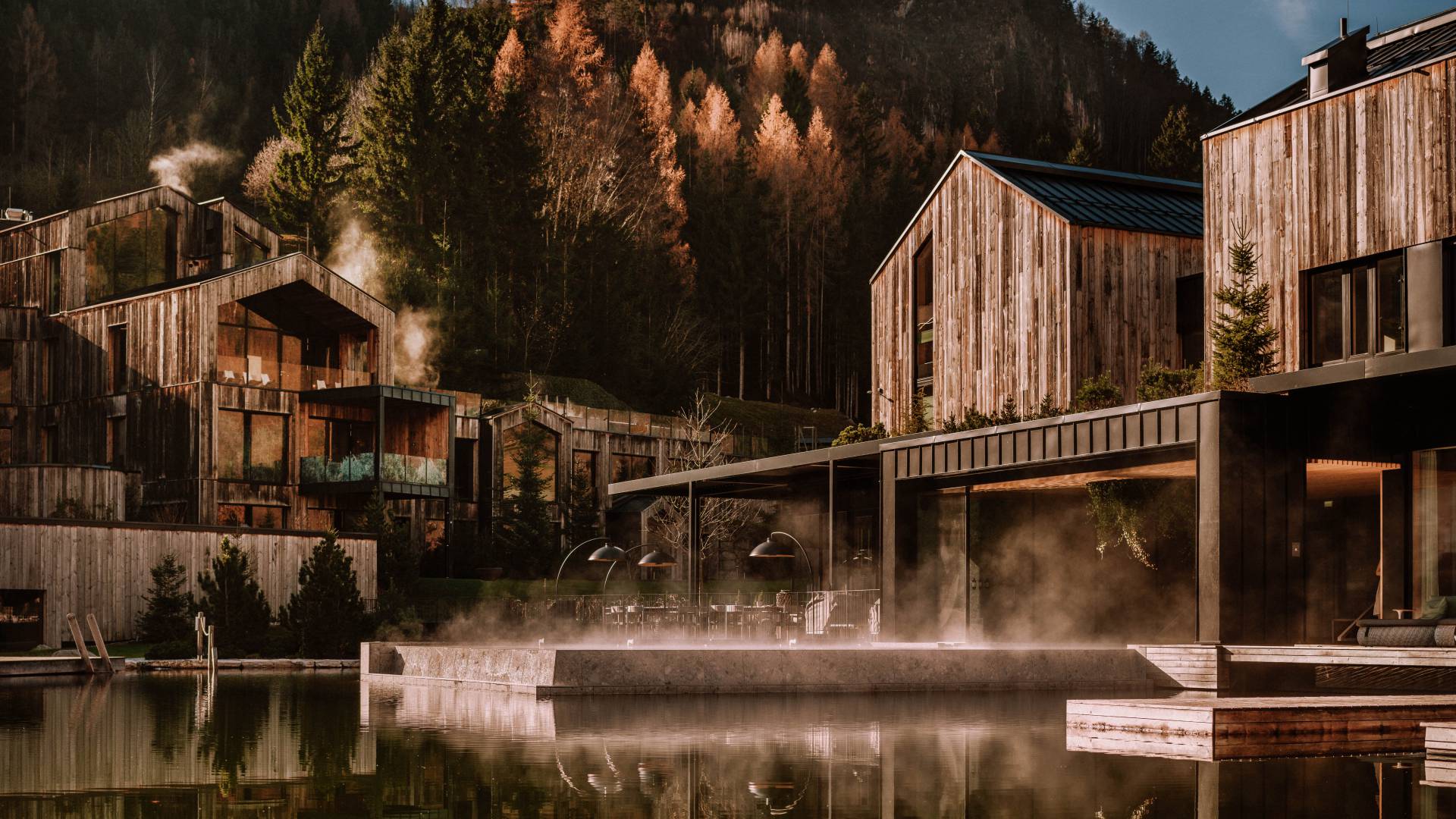 Naturhotel Forsthofgut mit dampfendem Seepool vor bewaldeten Bergen.