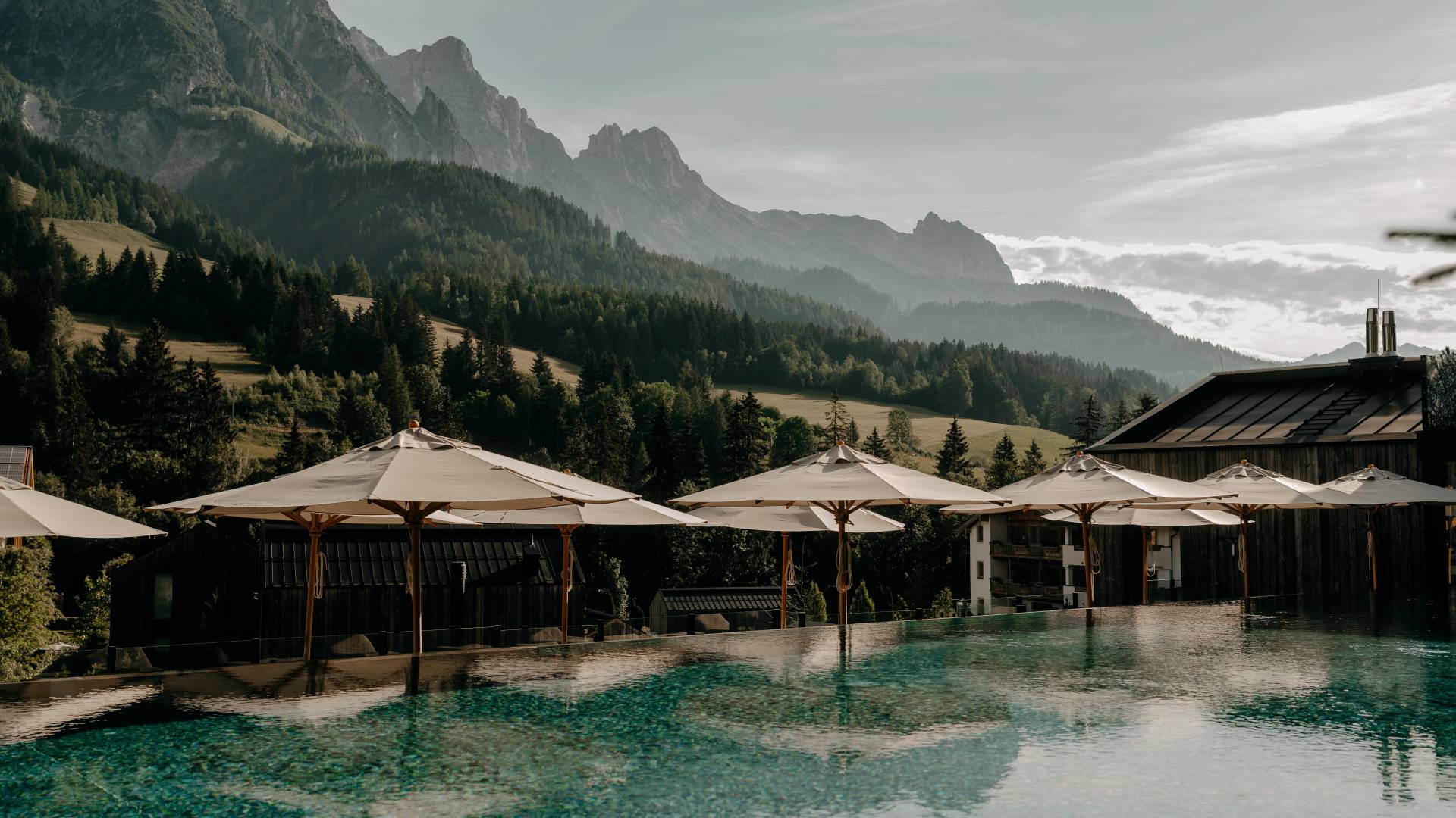 Sportpool mit Liegefläche, Sonnenschirmen und Blick auf die Leoganger Steinberge im Sommer.