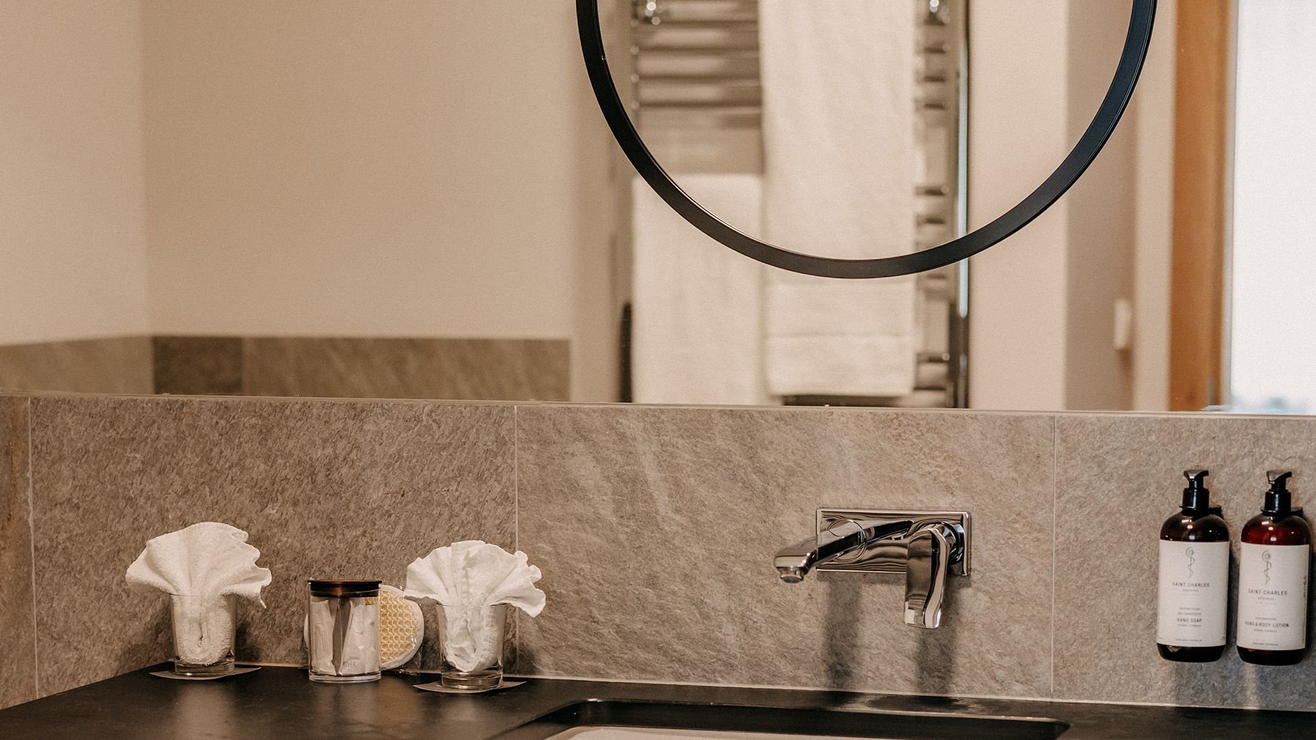 Modern bathroom featuring a sleek faucet and a large wall-mounted mirror. Above the large mirror there is a smaller round mirror.