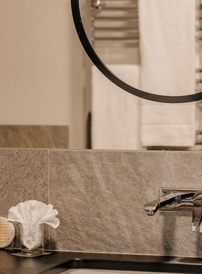 Modern bathroom featuring a sleek faucet and a large wall-mounted mirror. Above the large mirror there is a smaller round mirror.