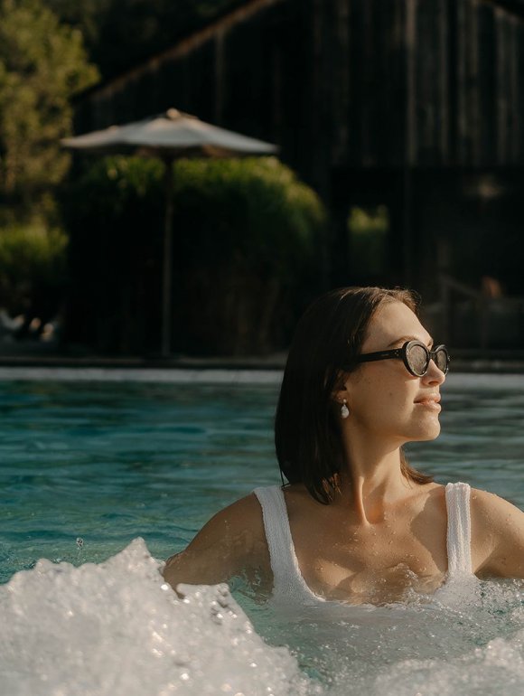 Smiling woman with glasses relaxing in an outdoor pool.