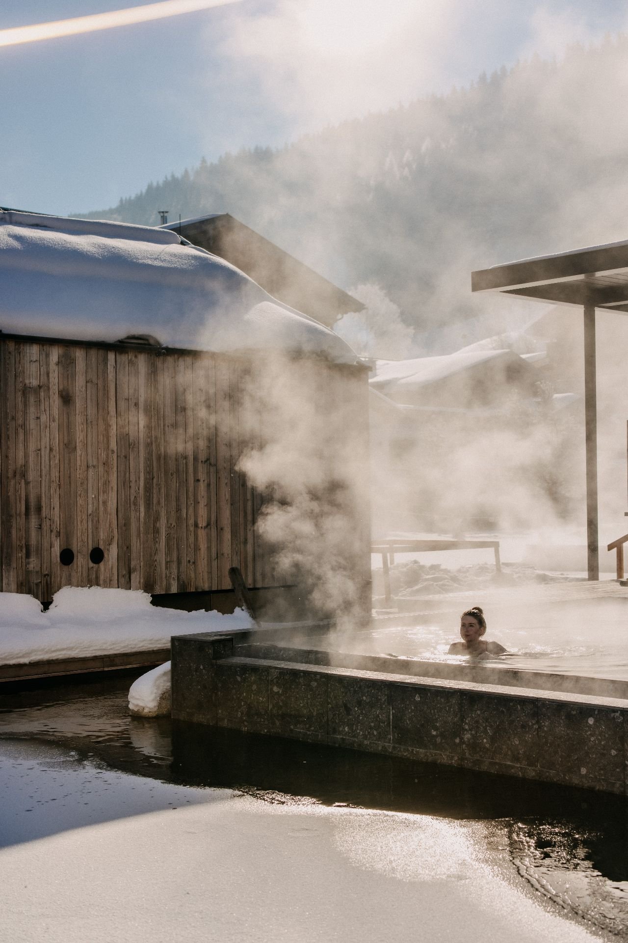 A guest relaxing in the steaming onsen pool at Forsthofgut, surrounded by snow-covered nature and an alpine winter landscape in Leogang.