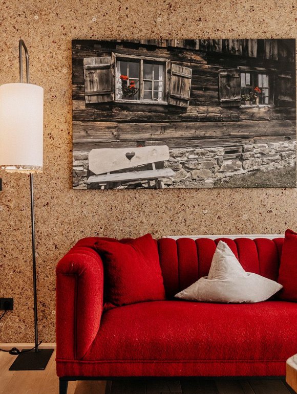 Section of a stylish furnished suite with a red couch, decorative pillows, and a black floor lamp. In the background, a children's room with a bunk bed is visible through an open door.