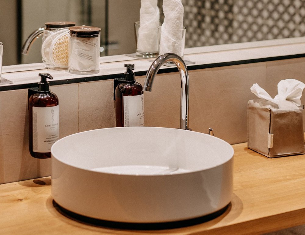 Detail view of a stylish hotel bathroom featuring a round countertop basin on a sleek vanity; next to it are premium hotel cosmetic products.