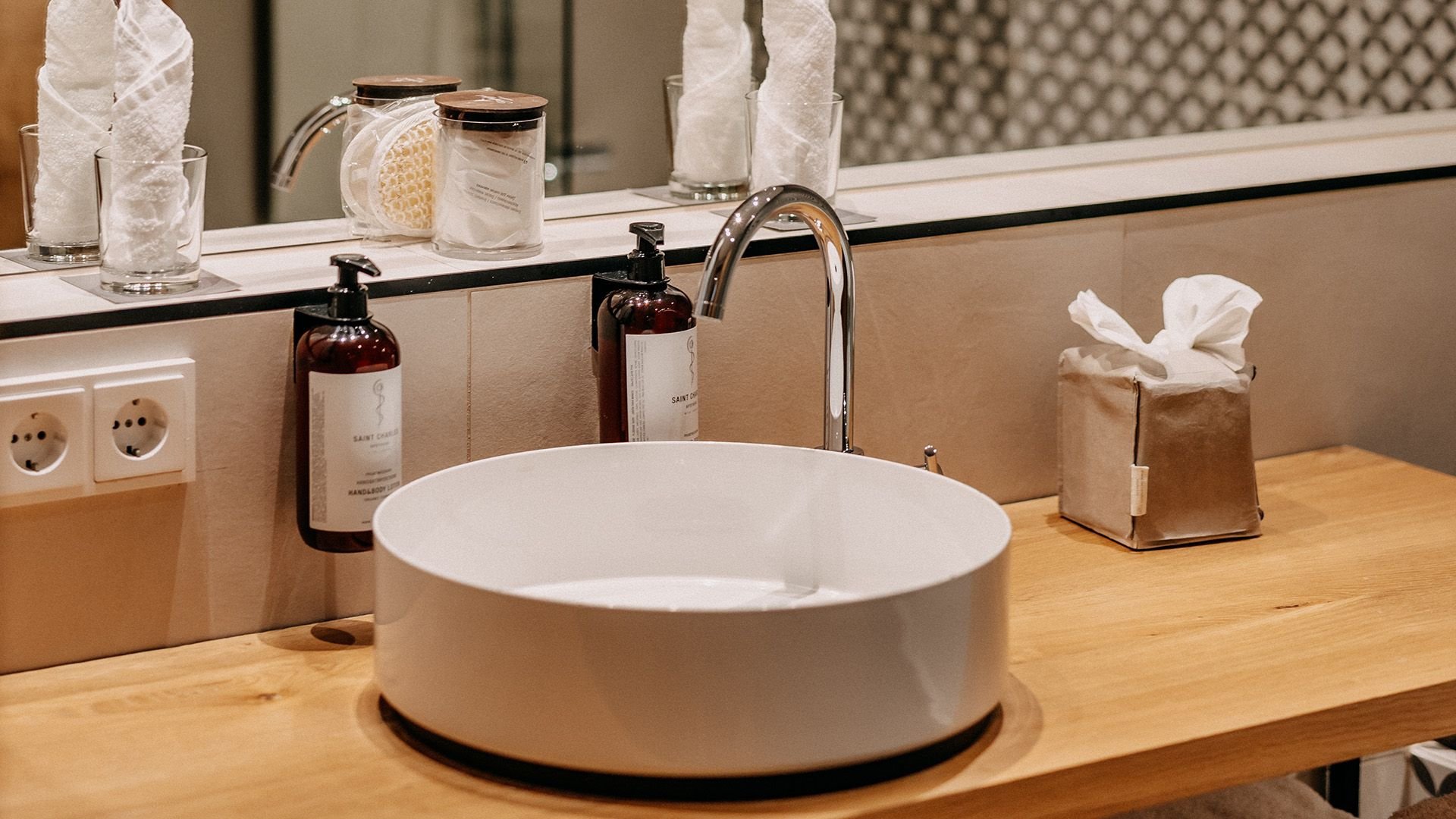 Detail view of a stylish hotel bathroom featuring a round countertop basin on a sleek vanity; next to it are premium hotel cosmetic products.