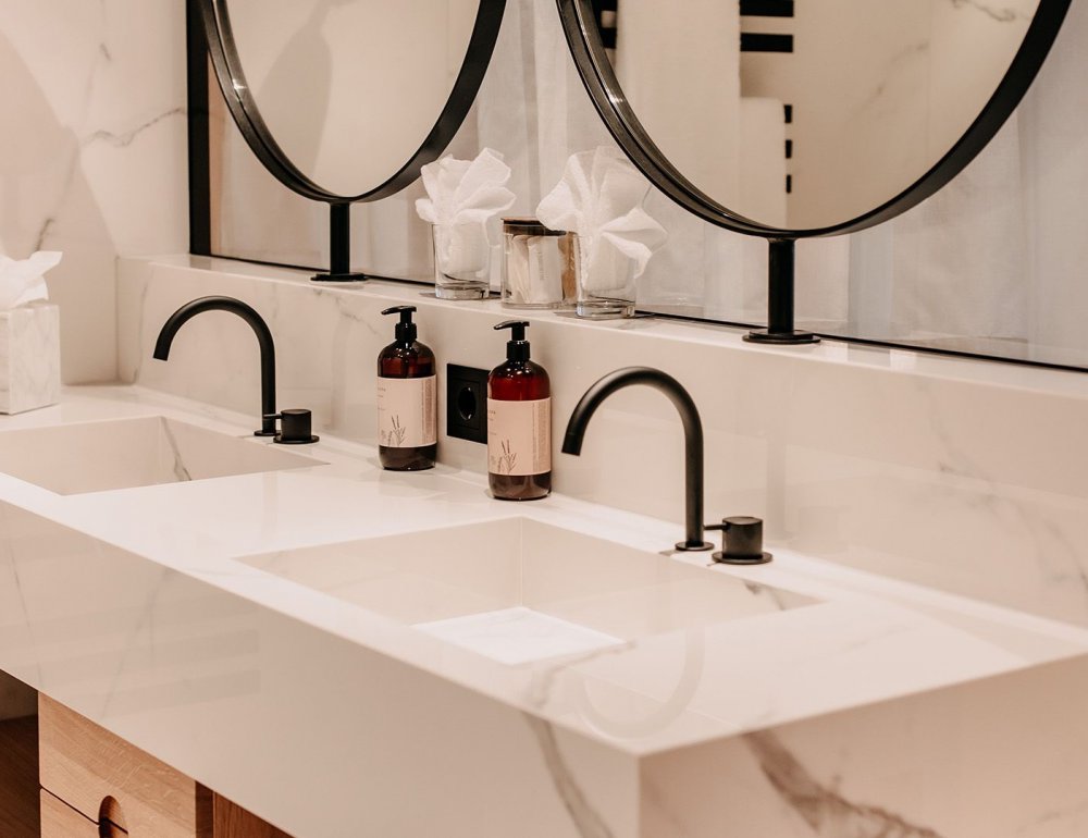Modern bathroom featuring white marble surfaces, sleek black fixtures, and a partial view of the mirror.