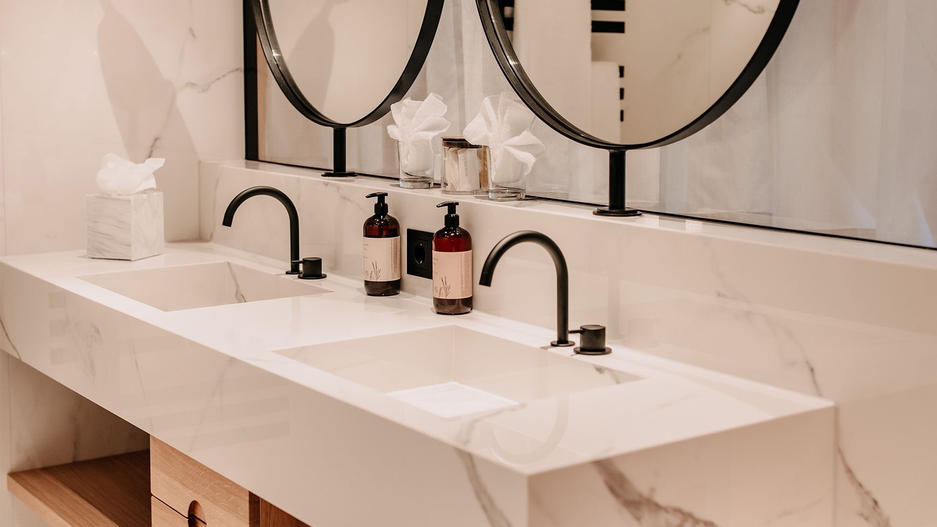 Modernes Badezimmer mit weißen Marmorflächen, eleganten schwarzen Armaturen und einem Ausschnitt des Spiegels.