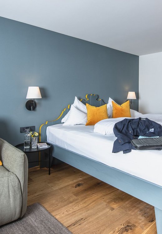 Bright “Landidyll” nature room with double bed, cosy sofa and wooden floor in front of a blue wall.