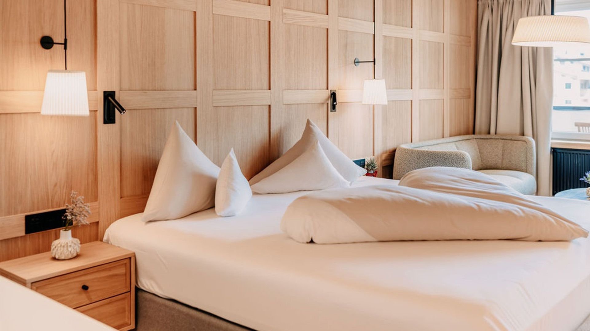 Cozy made bed in front of a wall with wood details, next to it a nightstand with a lamp.