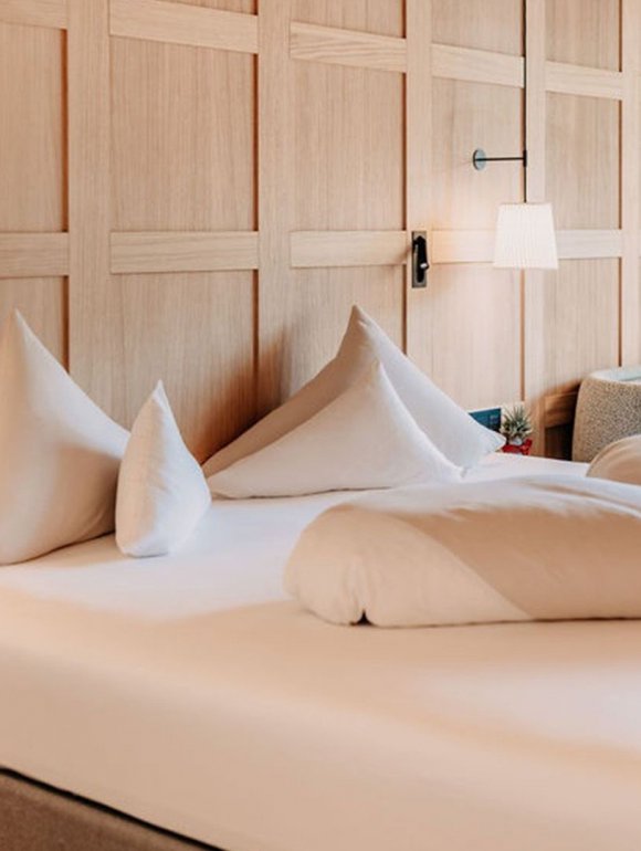 Cozy made bed in front of a wall with wood details, next to it a nightstand with a lamp.