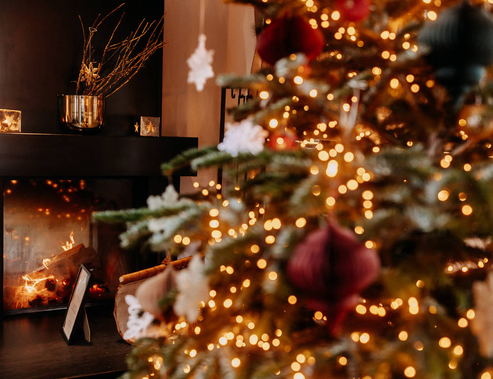 Festively decorated Christmas tree at Naturhotel Forsthofgut with a view of the fireplace in the background.