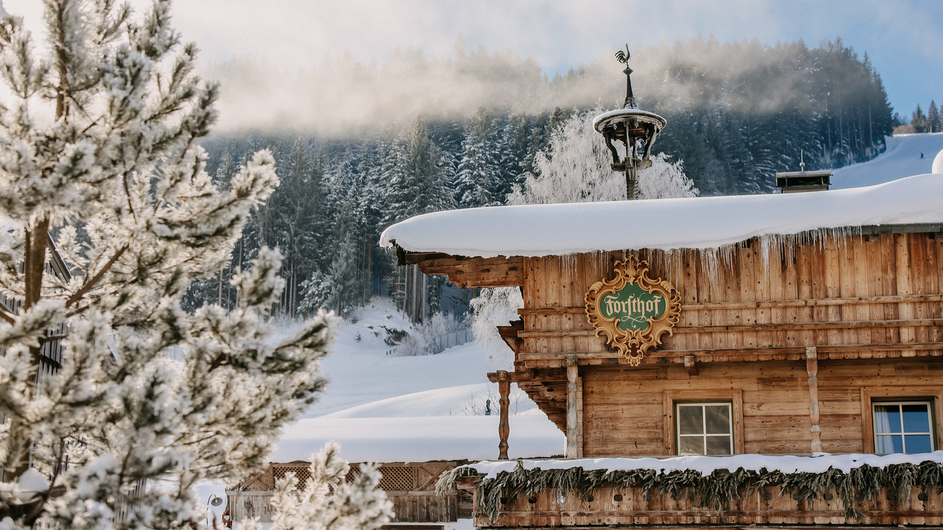 The snow-covered Forsthofgut Stammhaus in winter with mountains in the background.