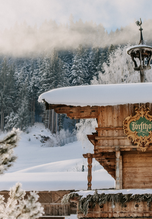 Das verschneite Stammhaus des Forsthofguts im Winter mit Bergen im Hintergrund.