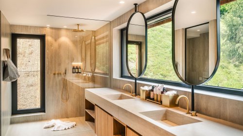 Bathroom with elegant gold modern fixtures and shower, suspended mirrors, and a large window.