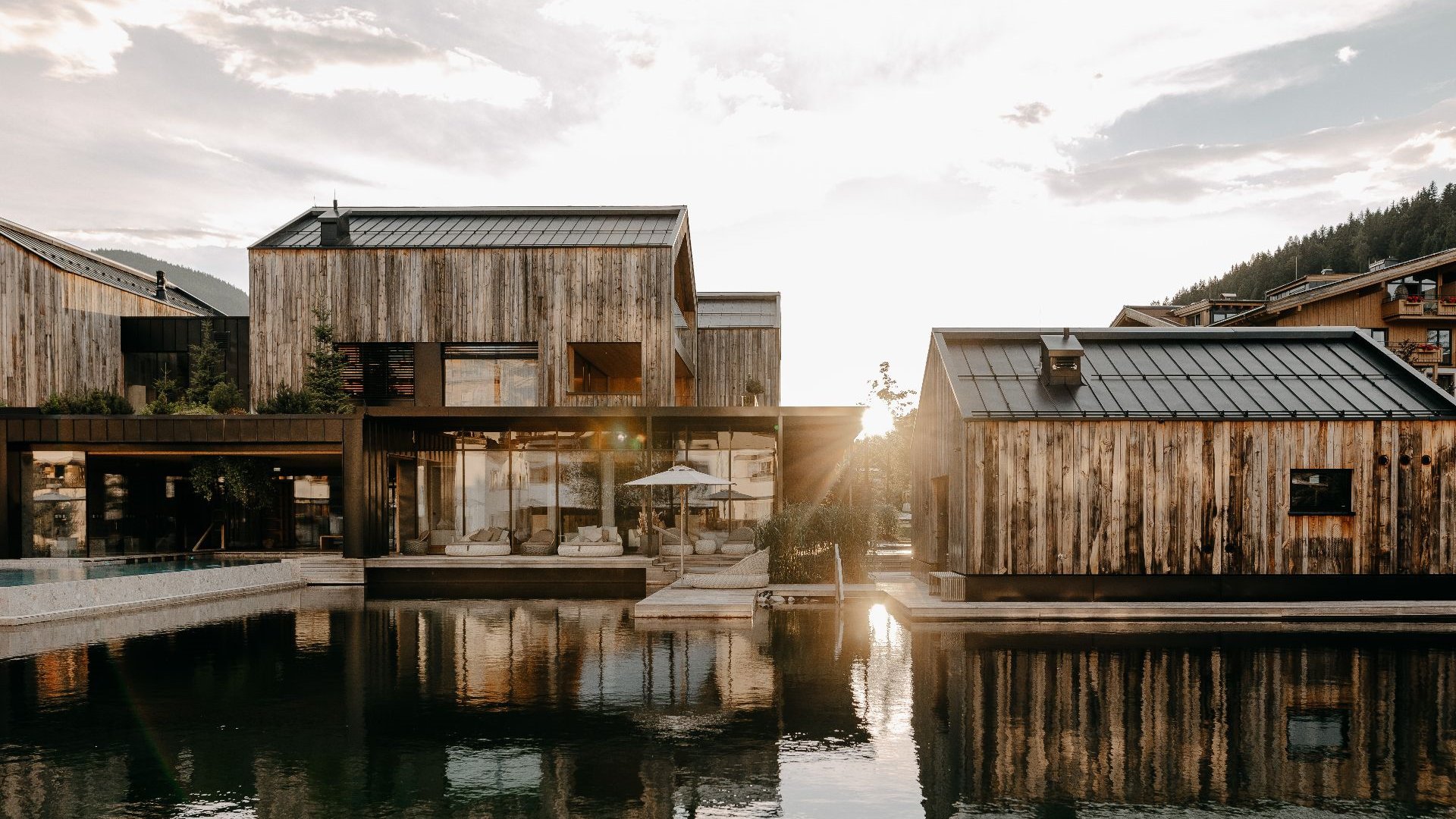 Sunset over the nature-inspired buildings of the Forsthofgut with a reflective water surface in the foreground