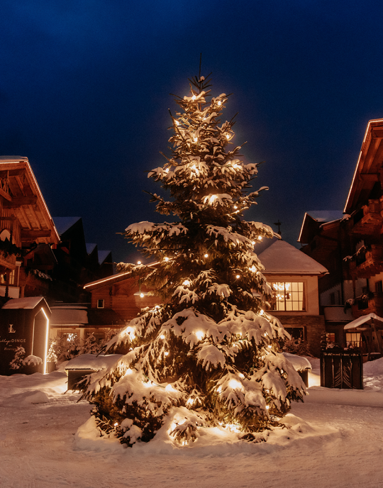 Weihnachtsbaum mit stimmungsvoller Beleuchtung im verschneiten Innenhof des Naturhotels Forsthofgut bei Abenddämmerung.
