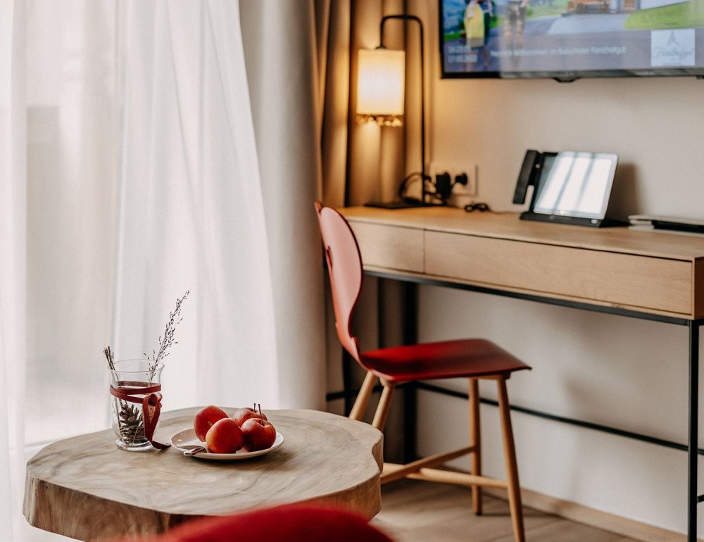 Decorated small table with a desk and an armchair behind it. Above the desk, a television is mounted on the wall.