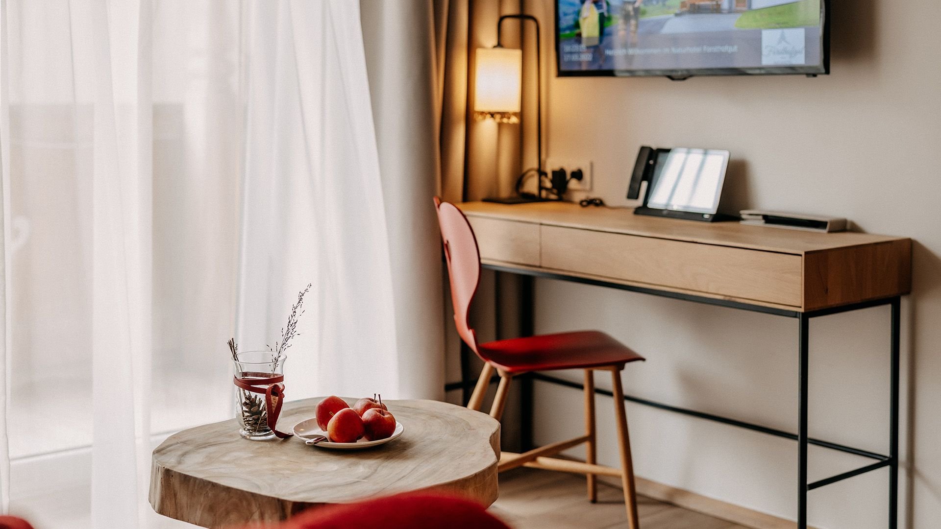 Decorated small table with a desk and an armchair behind it. Above the desk, a television is mounted on the wall.