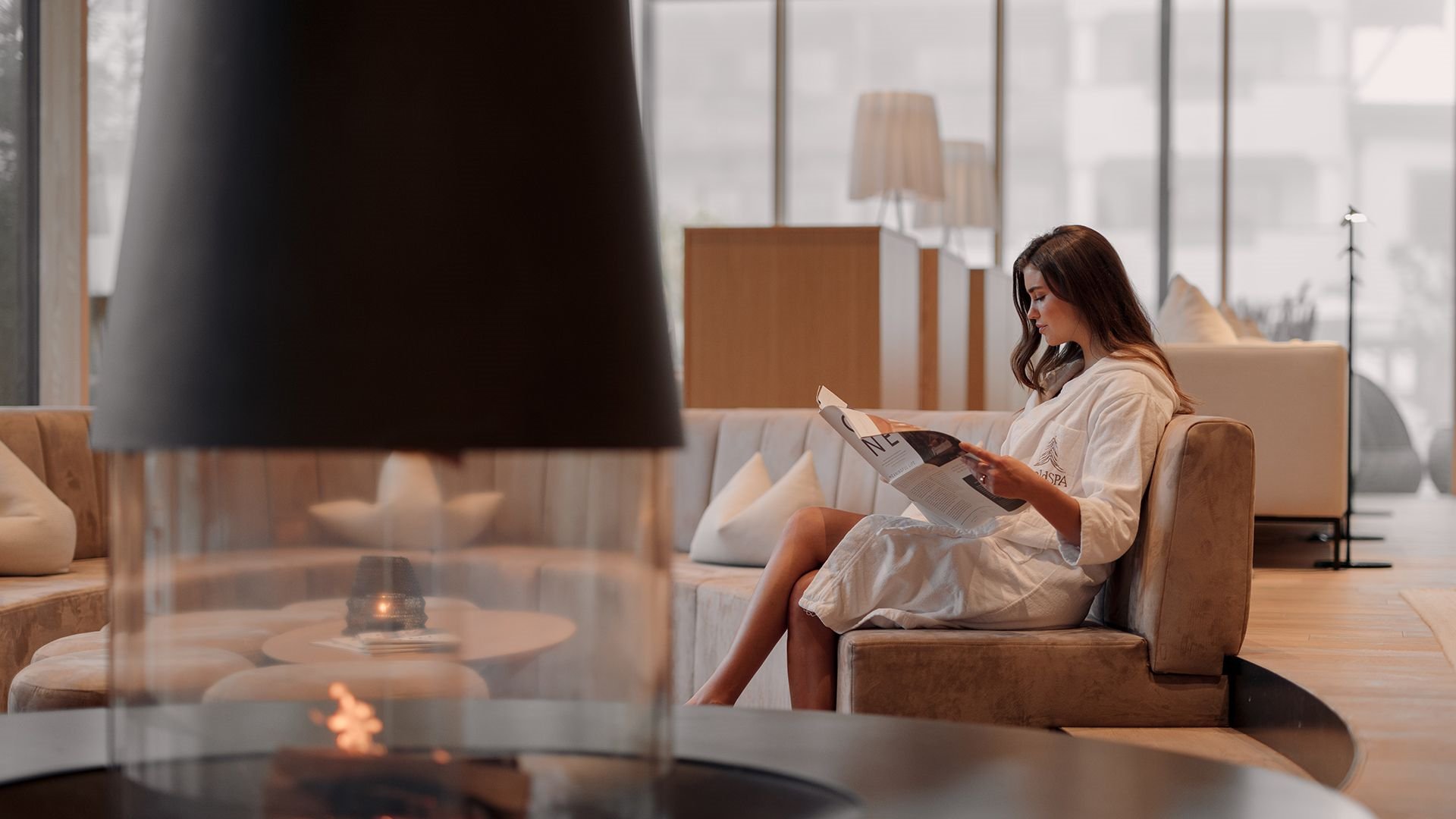 A woman relaxes in the relaxation room at the Naturhotel Forsthofgut, reading a book in front of the fireplace.