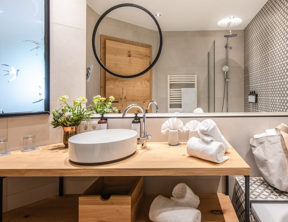 Bathroom with a freestanding sink, a large mirror above it, and a small round mirror. To the left of the counter is a bathtub.