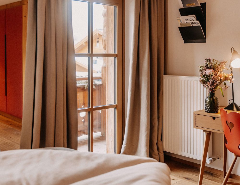 Partial view of a hotel room with the edge of a bed in the foreground and a desk with a chair in the background.