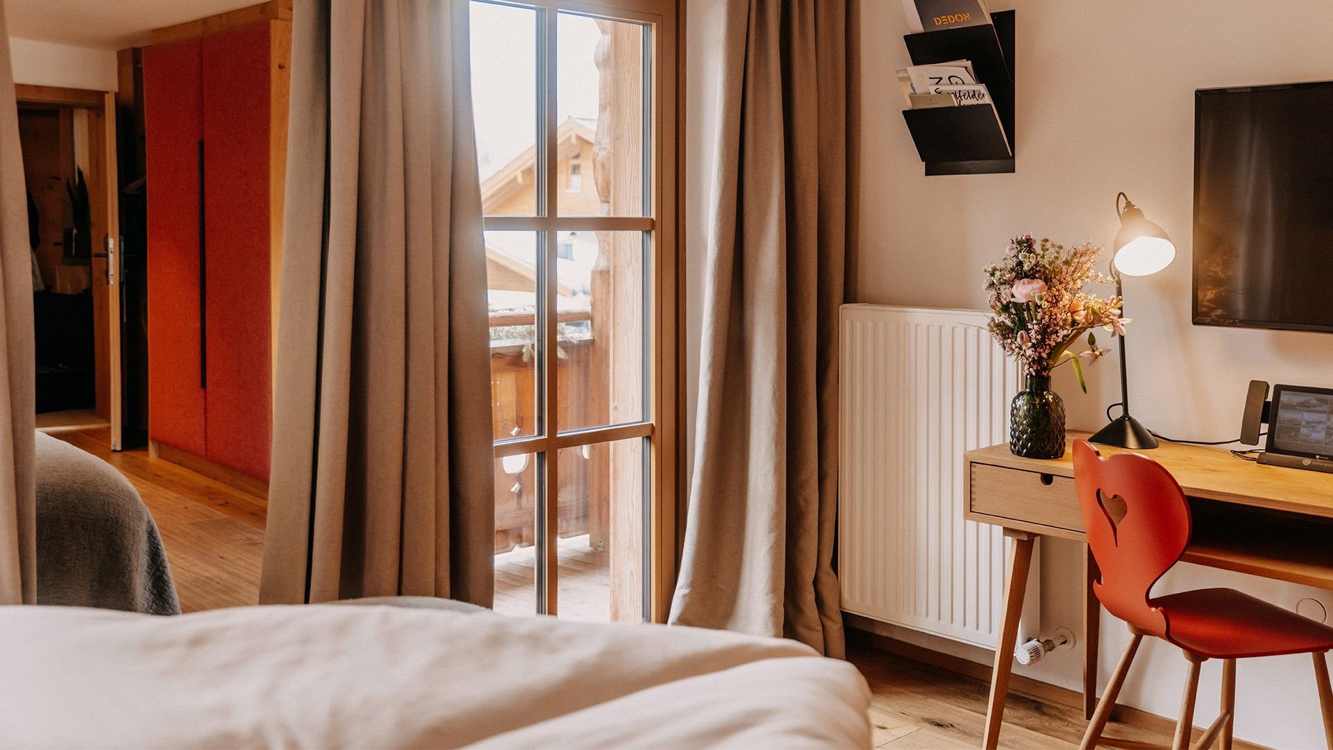 Partial view of a hotel room with the edge of a bed in the foreground and a desk with a chair in the background.
