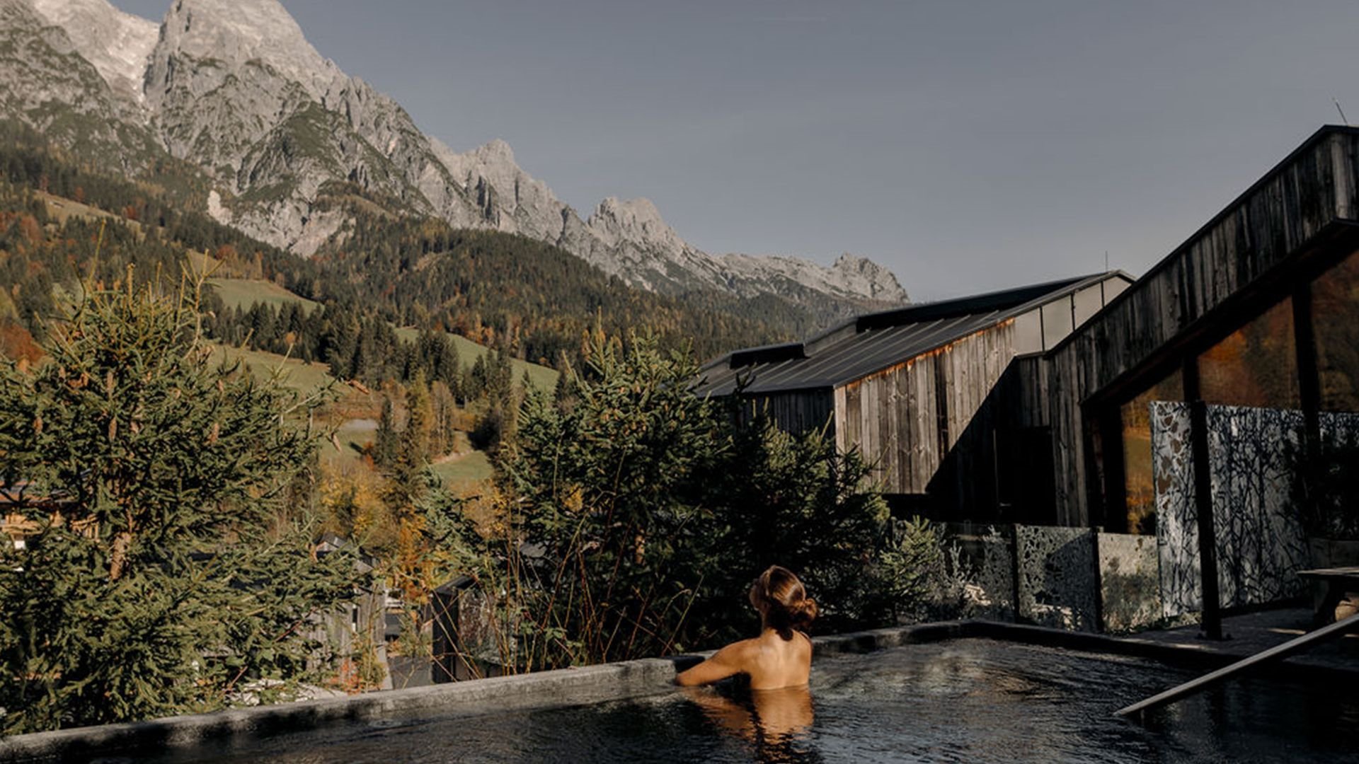 Frau entspannt im Whirlpool des Forsthofguts mit Blick auf die umliegenden Berge und Wälder.