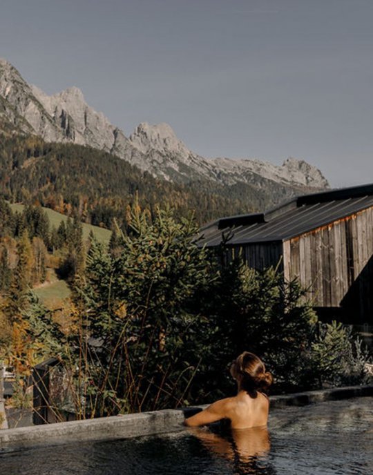 Frau entspannt im Whirlpool des Forsthofguts mit Blick auf die umliegenden Berge und Wälder.