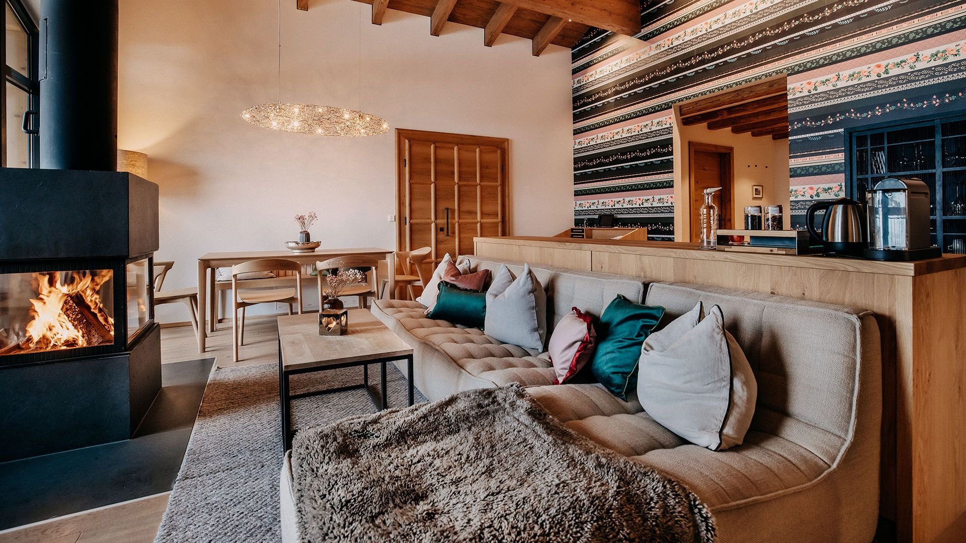 Wohnbereich aus einer anderen Perspektive mit gemütlich brennendem Kamin und einem Esstisch, der im Hintergrund steht.