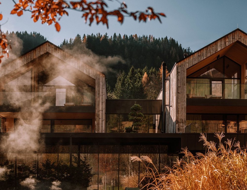 Herbstliche Außenansicht der Seehäuse vom Naturhotel Forsthofgut mit aufsteigendem Dampf.