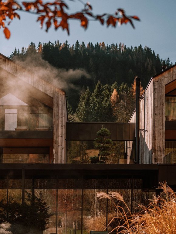 Autumnal exterior view of the lake houses at the Naturhotel Forsthofgut with rising steam.
