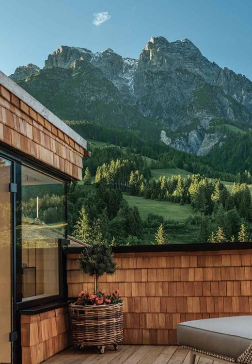 Exclusive rooftop terrace featuring a private wooden sauna, hot tub, and inviting seating areas, with impressive mountain views and vistas of lush alpine meadows. The panorama invites guests to relax and enjoy the beauty of the alpine nature.