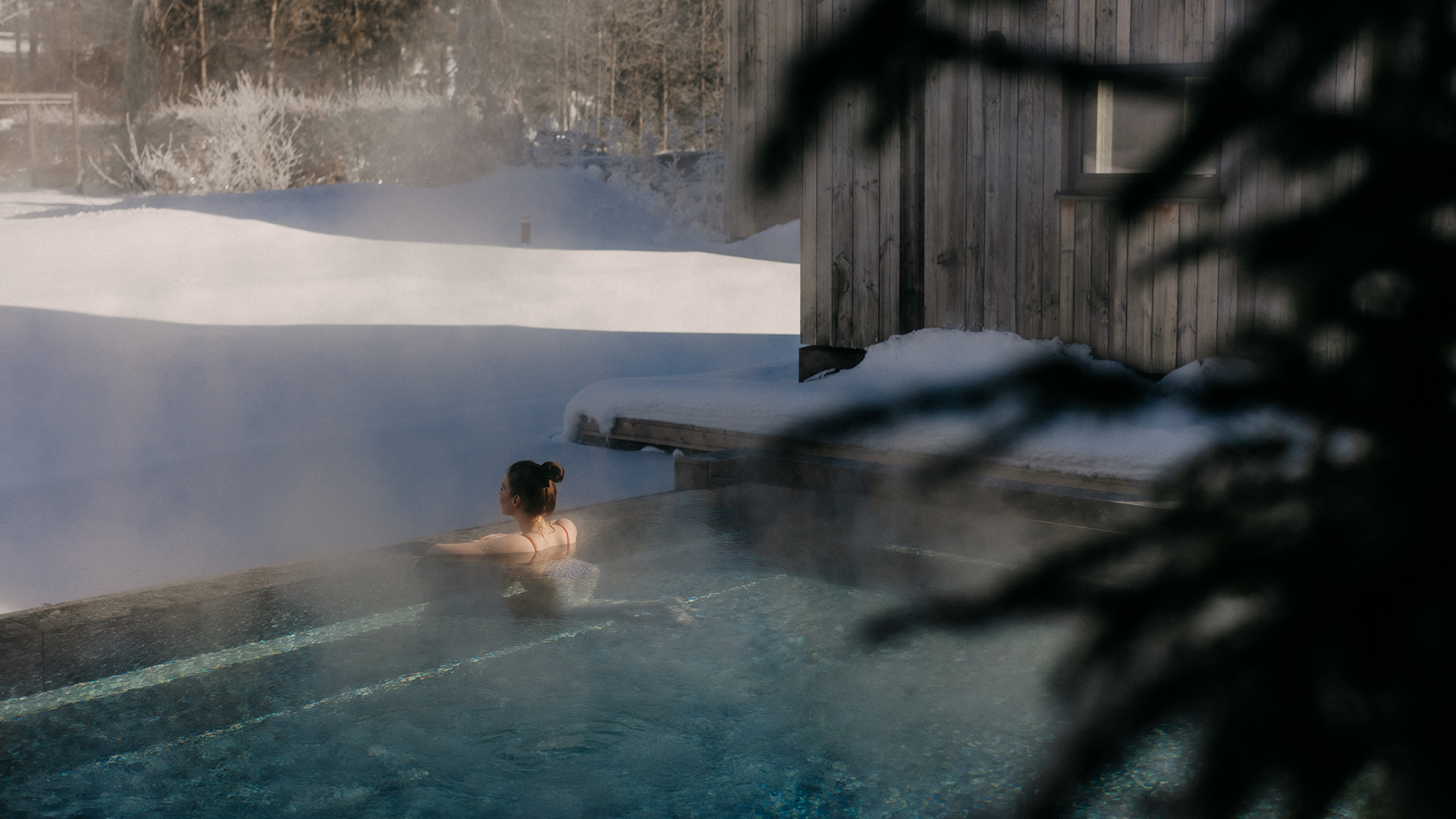 Gast im dampfenden Onsen-Pool, umgeben von tief verschneiter Winterlandschaft.
