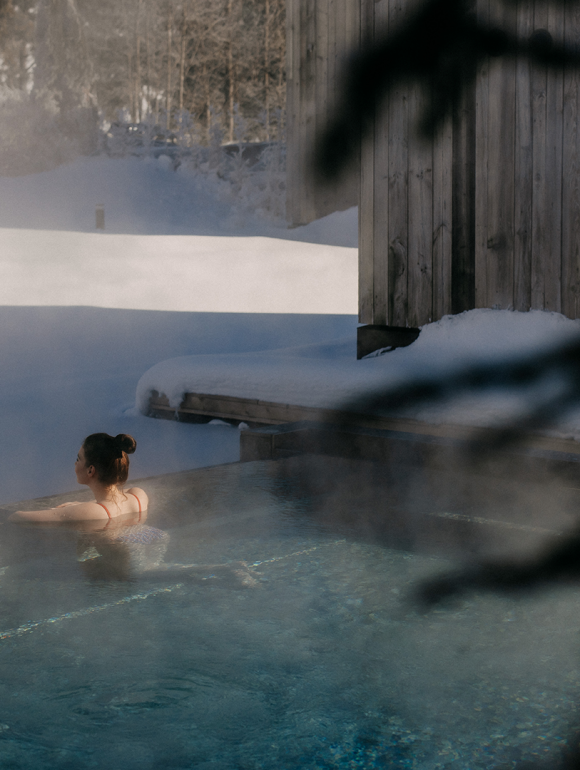 Gast im dampfenden Onsen-Pool, umgeben von tief verschneiter Winterlandschaft.